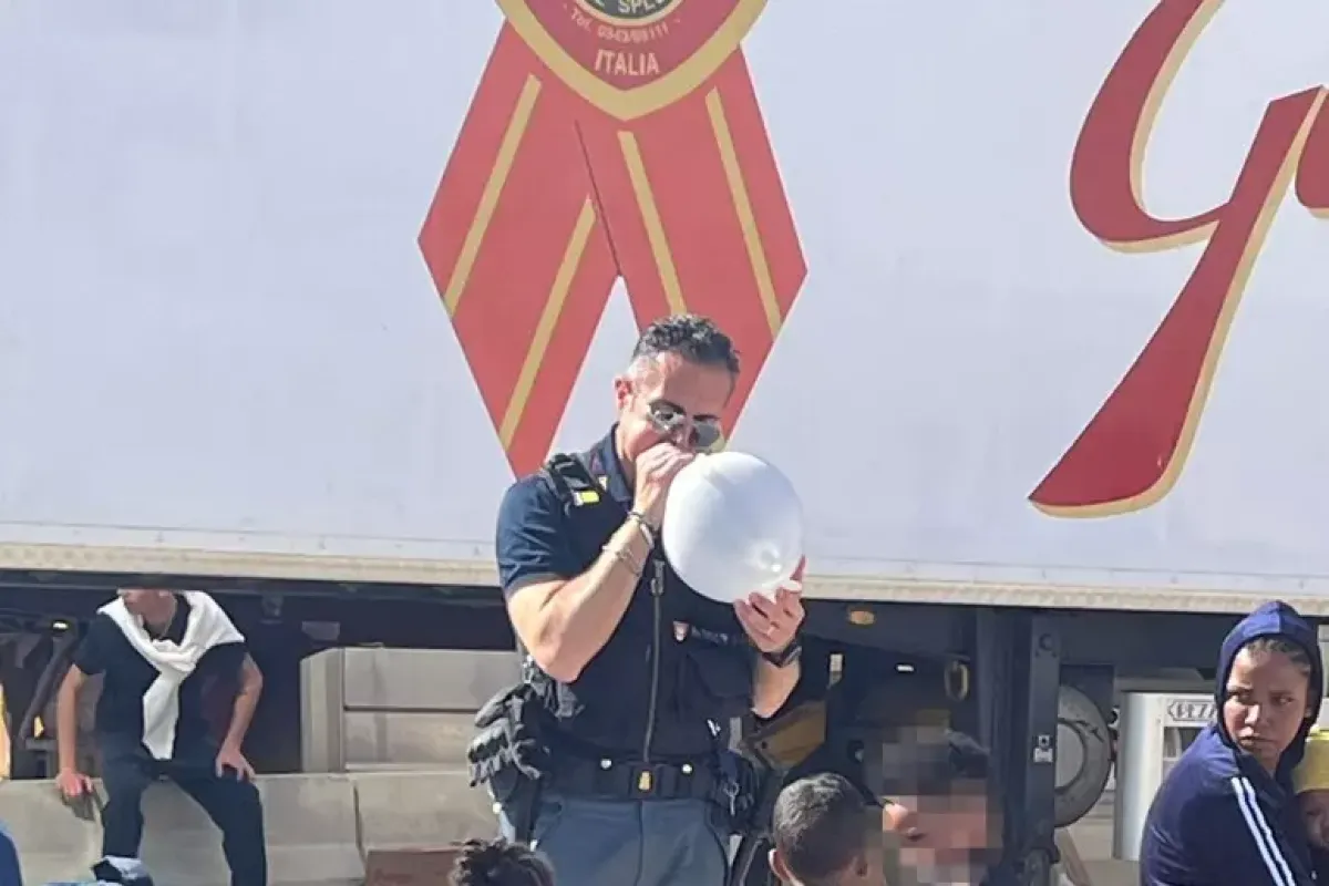 Poliziotto regala palloncini ai migranti in attesa al porto - Credit foto: Ansa